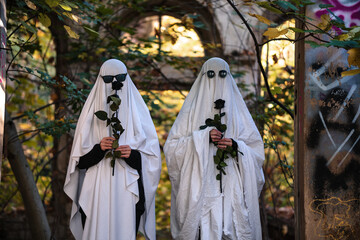 A funny image of two people with black roses in ghost costumes and sunglasses in an abandoned building