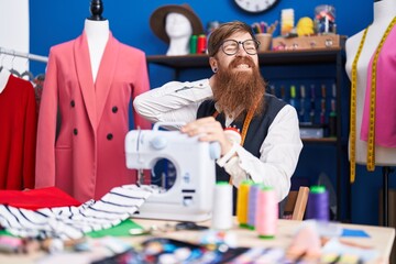 Poster - Young redhead man tailor stressed using sewing machine at clothing factory