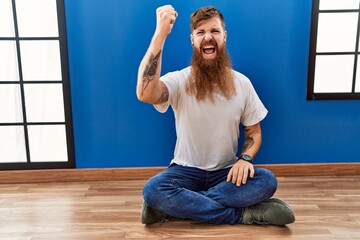 Sticker - Redhead man with long beard sitting on the floor at empty room angry and mad raising fist frustrated and furious while shouting with anger. rage and aggressive concept.