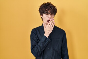 Sticker - Young man wearing glasses over yellow background bored yawning tired covering mouth with hand. restless and sleepiness.