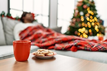 Poster - Young african american man sleeping lying on the sofa by christmas tree at home.