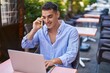 © Krakenimages.com - Young hispanic man using laptop talking on smartphone sitting on table at coffee shop terrace