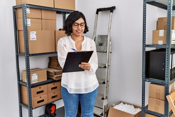 Poster - Young latin woman ecommerce business worker writing on clipboard at office