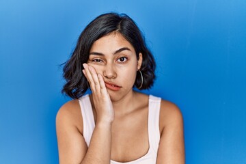 Poster - Young hispanic woman standing over blue background thinking looking tired and bored with depression problems with crossed arms.