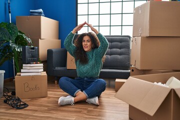 Canvas Print - Young hispanic woman sitting on the floor at new home clueless and confused expression. doubt concept.