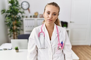 Poster - Young caucasian woman wearing doctor uniform and stethoscope at the clinic relaxed with serious expression on face. simple and natural looking at the camera.