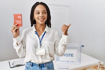 Wall Mural - Young african american woman at political campaign election holding swiss passport pointing thumb up to the side smiling happy with open mouth