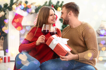 Poster - Happy young couple with glasses of wine at gift at home on Christmas eve