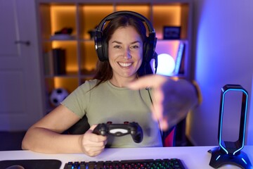 Wall Mural - Beautiful brunette woman playing video games wearing headphones smiling friendly offering handshake as greeting and welcoming. successful business.