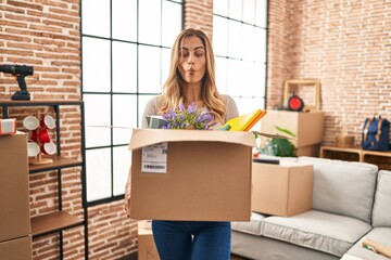 Sticker - Young blonde woman moving to a new home holding cardboard box making fish face with mouth and squinting eyes, crazy and comical.