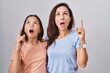 © Krakenimages.com - Young mother and daughter standing over white background amazed and surprised looking up and pointing with fingers and raised arms.