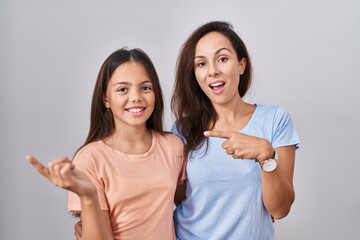 Sticker - Young mother and daughter standing over white background with a big smile on face, pointing with hand finger to the side looking at the camera.