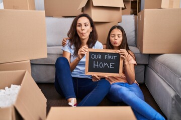 Wall Mural - Young mother and daughter sitting on the floor at new home making fish face with mouth and squinting eyes, crazy and comical.