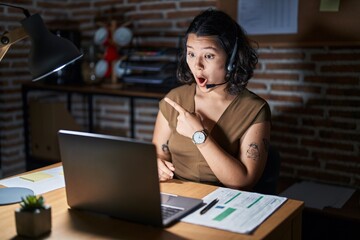 Poster - Young hispanic woman working at the office at night surprised pointing with finger to the side, open mouth amazed expression.