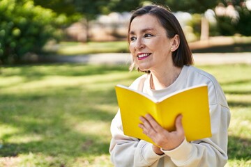 Sticker - Middle age woman reading book sitting on herb at park