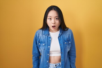 Poster - Young asian woman standing over yellow background afraid and shocked with surprise and amazed expression, fear and excited face.