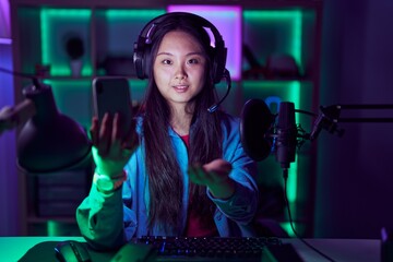 Wall Mural - Young asian woman playing video games with smartphone smiling cheerful offering palm hand giving assistance and acceptance.