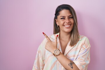 Wall Mural - Blonde woman standing over pink background cheerful with a smile of face pointing with hand and finger up to the side with happy and natural expression on face