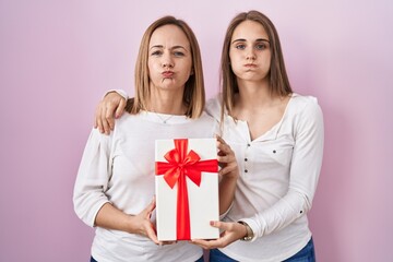 Poster - Middle age mother and young daughter holding mothers day gift puffing cheeks with funny face. mouth inflated with air, catching air.