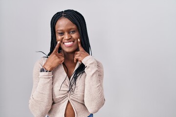 Sticker - African woman with braids standing over white background smiling with open mouth, fingers pointing and forcing cheerful smile