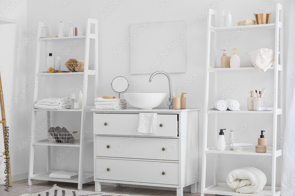 Shelf units with bath accessories and modern sink near white wall in bathroom interior