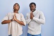 © Krakenimages.com - Young african american couple standing over blue background together begging and praying with hands together with hope expression on face very emotional and worried. begging.