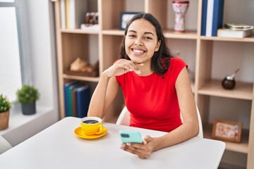 Young african american woman using smartphone drinking coffee at home