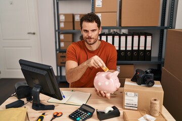 Canvas Print - Young hispanic man working at small business ecommerce holding piggy bank skeptic and nervous, frowning upset because of problem. negative person.