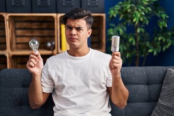 Canvas Print - Hispanic man holding led lightbulb and incandescent bulb skeptic and nervous, frowning upset because of problem. negative person.