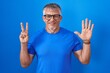 © Krakenimages.com - Hispanic man with grey hair standing over blue background showing and pointing up with fingers number seven while smiling confident and happy.