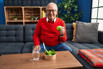 Poster - Senior man with grey hair eating salad and green apple looking positive and happy standing and smiling with a confident smile showing teeth