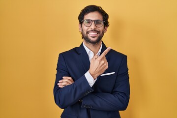 Poster - Handsome latin man standing over yellow background with a big smile on face, pointing with hand finger to the side looking at the camera.