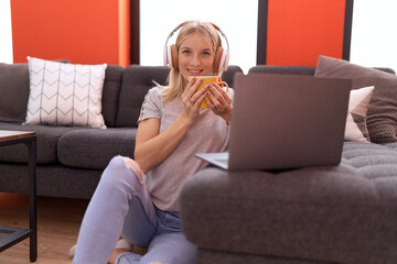 Poster - Young blonde woman watching video on laptop drinking coffee at home