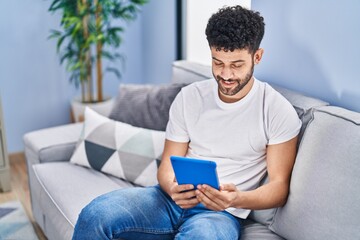 Sticker - Young arab man using touchpad sitting on sofa at home