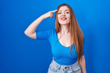 Sticker - Redhead woman standing over blue background smiling pointing to head with one finger, great idea or thought, good memory