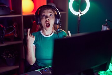 Poster - Redhead woman playing video games amazed and surprised looking up and pointing with fingers and raised arms.