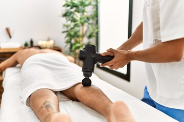 Wall Mural - Two hispanic men physiotherapist and patient massaging legs using percussion gun at beauty center