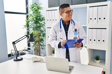 Wall Mural - Young latin man doctor writing on medical report standing at clinic