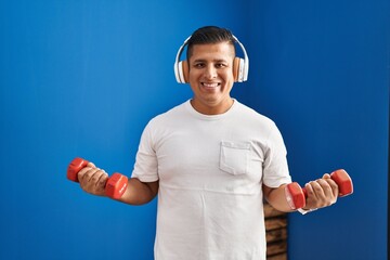 Poster - Young latin man listening to music using dumbbells training at sport center