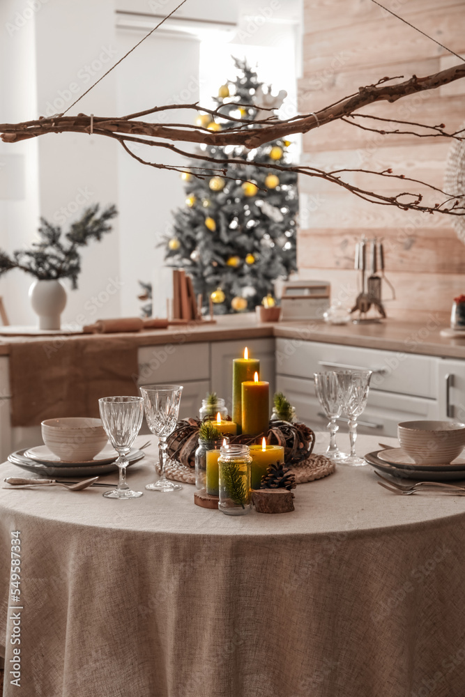 Christmas table setting with burning candles and wreath in kitchen