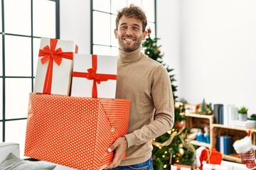 Poster - Young hispanic man smiling confident holding christmas gifts at home