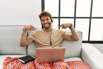 Canvas Print - Young handsome man with beard wearing operator headset working from home looking confident with smile on face, pointing oneself with fingers proud and happy.