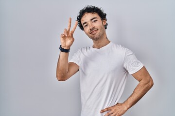 Sticker - Hispanic man standing over isolated background smiling looking to the camera showing fingers doing victory sign. number two.