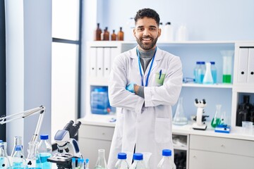 Wall Mural - Young hispanic man wearing scientist uniform standing with arms crossed gesture at laboratory