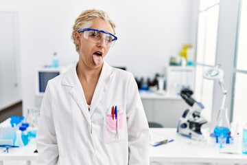 Poster - Middle age blonde woman working at scientist laboratory sticking tongue out happy with funny expression. emotion concept.