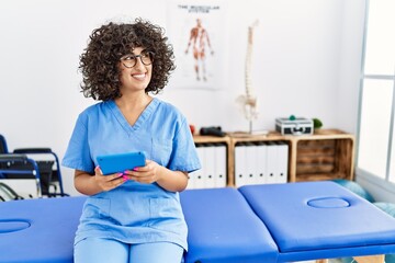 Poster - Young middle east woman wearing physio therapist uniform using touchpad at clinic