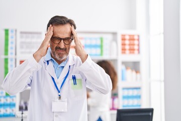 Poster - Middle age hispanic man working at pharmacy drugstore with hand on head, headache because stress. suffering migraine.