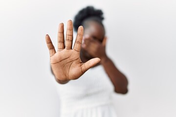 Sticker - Young african woman standing over white isolated background covering eyes with hands and doing stop gesture with sad and fear expression. embarrassed and negative concept.