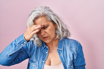 Poster - Middle age woman with grey hair standing over pink background tired rubbing nose and eyes feeling fatigue and headache. stress and frustration concept.