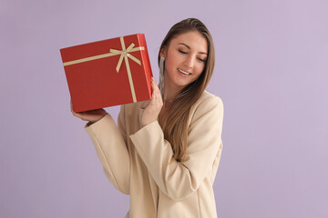 Sticker - Young woman in blazer with Christmas gift on lilac background